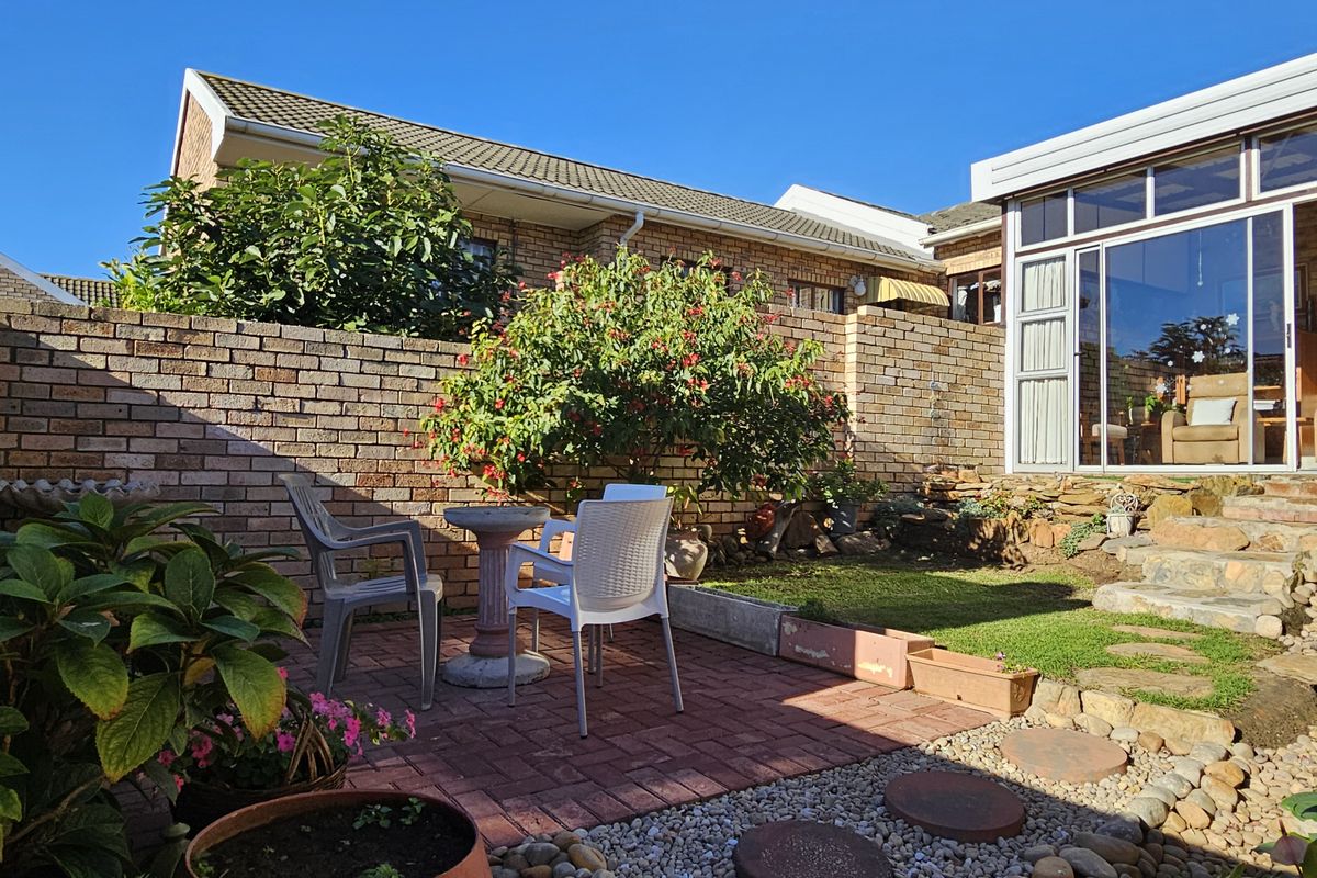A private rear courtyard featuring a paved patio area, stone retaining wall, and access to an attached sunroom with large glass windows.