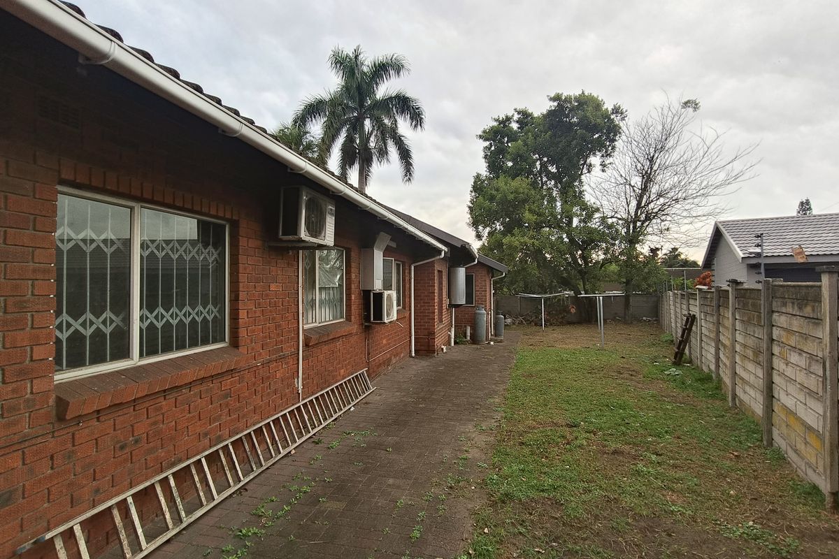 Rear exterior view of the house featuring a brick facade, paved walkway, and a spacious backyard with a concrete boundary wall.