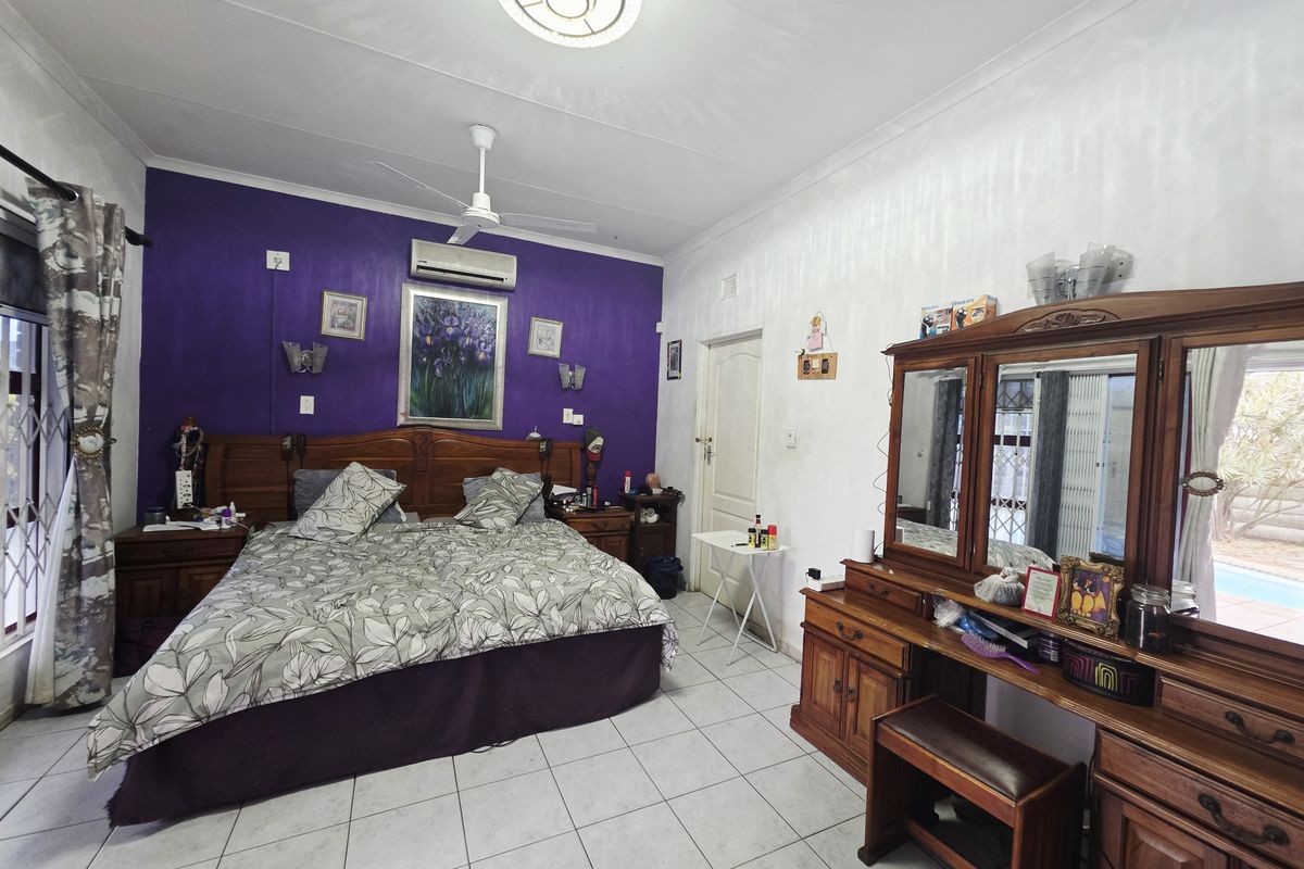 Spacious bedroom featuring tiled flooring, a ceiling fan, and a wall-mounted air conditioning unit, with direct access to the exterior via a security gate.
