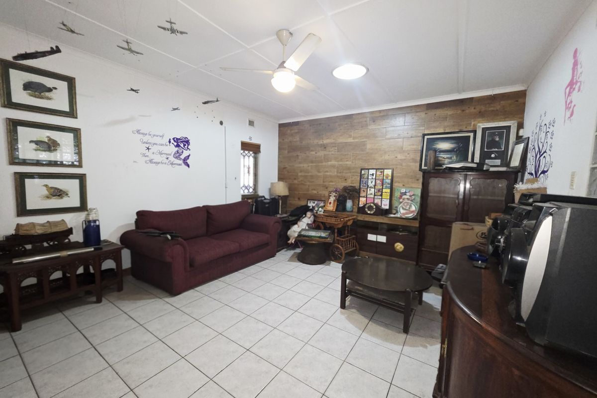 A living room featuring tiled flooring, a ceiling fan, and a wood-paneled feature wall, offering a functional space with potential for modernization.