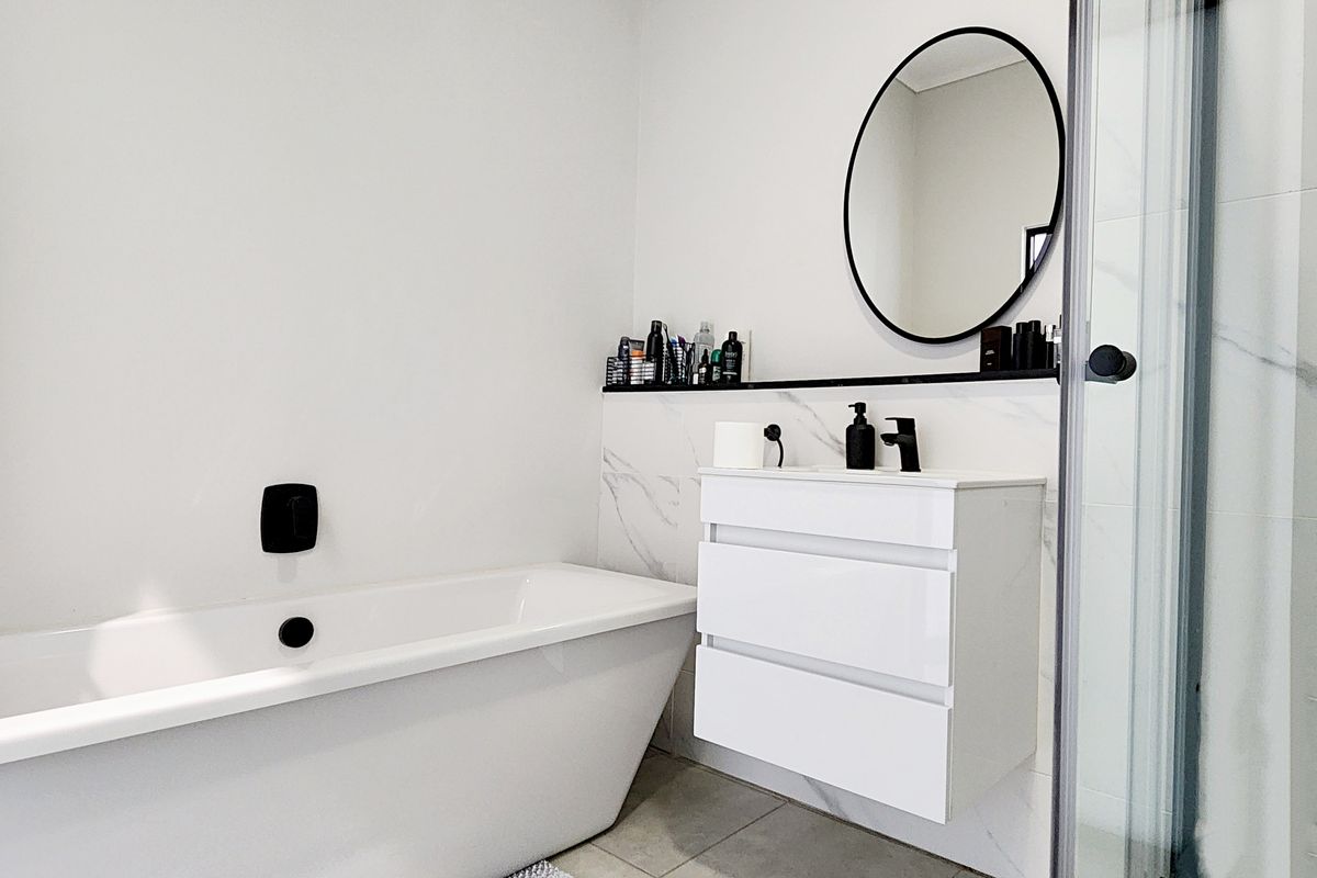Modern bathroom featuring a sleek freestanding bathtub, wall-mounted vanity with storage, and a glass-enclosed shower with marble-look wall tiles.