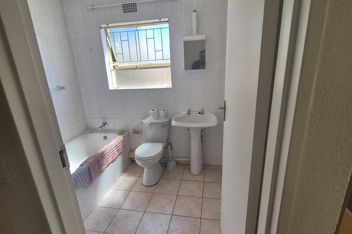 A functional bathroom featuring a bathtub, pedestal sink, and toilet with tiled finishes throughout. The space is ready for modernization.