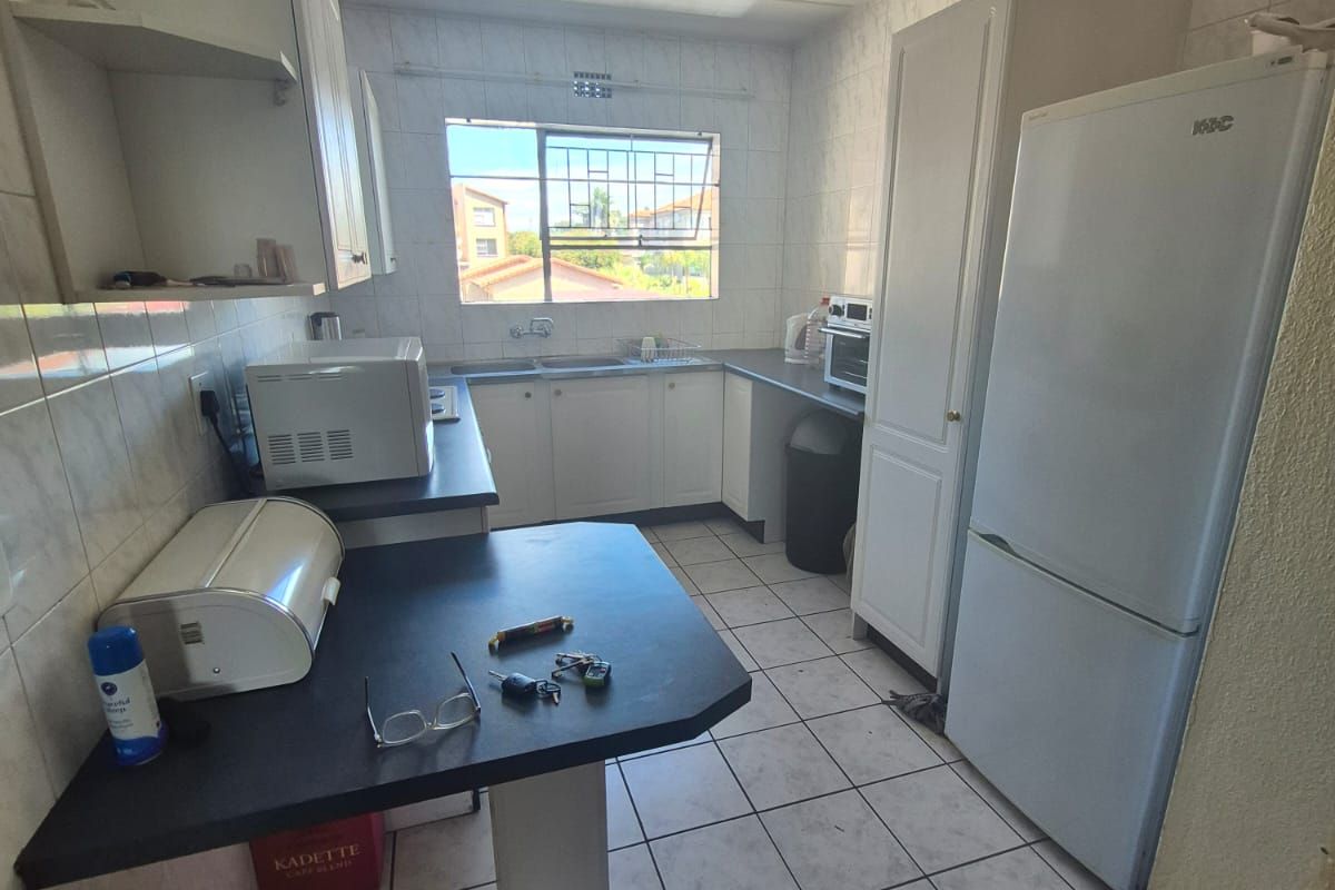 A functional kitchen featuring white built-in cabinetry, dark laminate countertops, tiled flooring, and a window providing natural light.