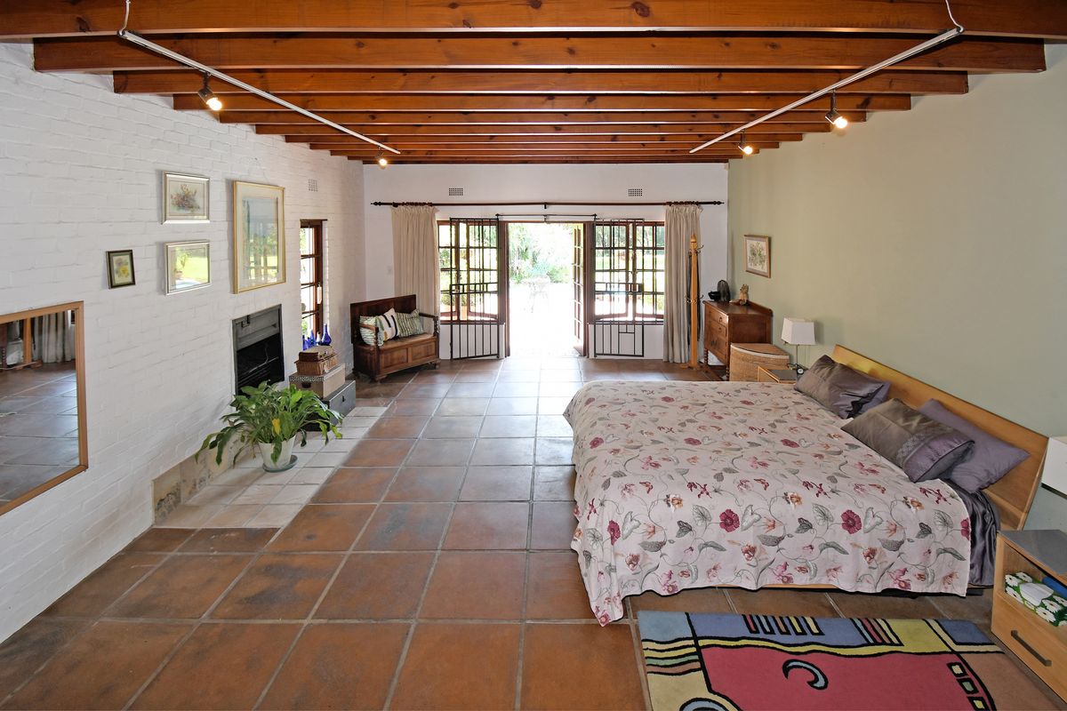 Spacious bedroom featuring exposed timber ceiling beams, a built-in fireplace, and double doors opening to the garden.