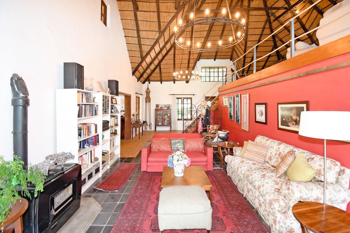 Spacious living room featuring a high vaulted thatched ceiling, exposed timber beams, a built-in fireplace, and a mezzanine level overlooking the main area.