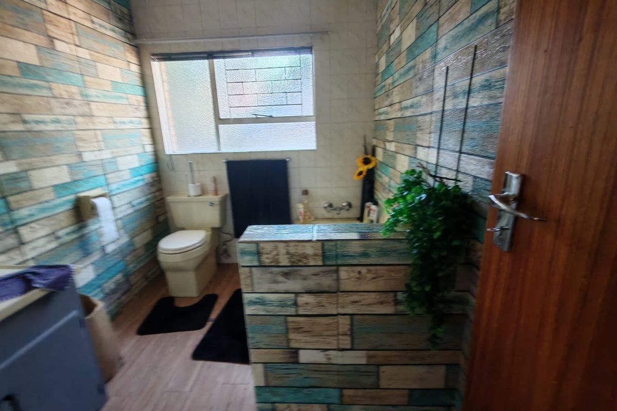 A compact bathroom featuring a toilet, vanity, and window, finished with decorative wood-look wall paneling.