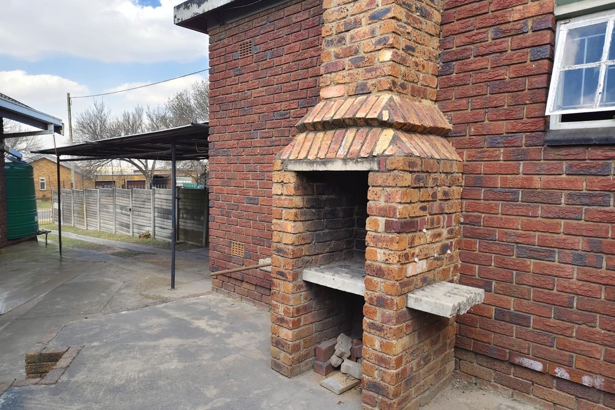 Rear exterior area featuring a traditional brick fireplace, concrete patio, and a covered carport structure.