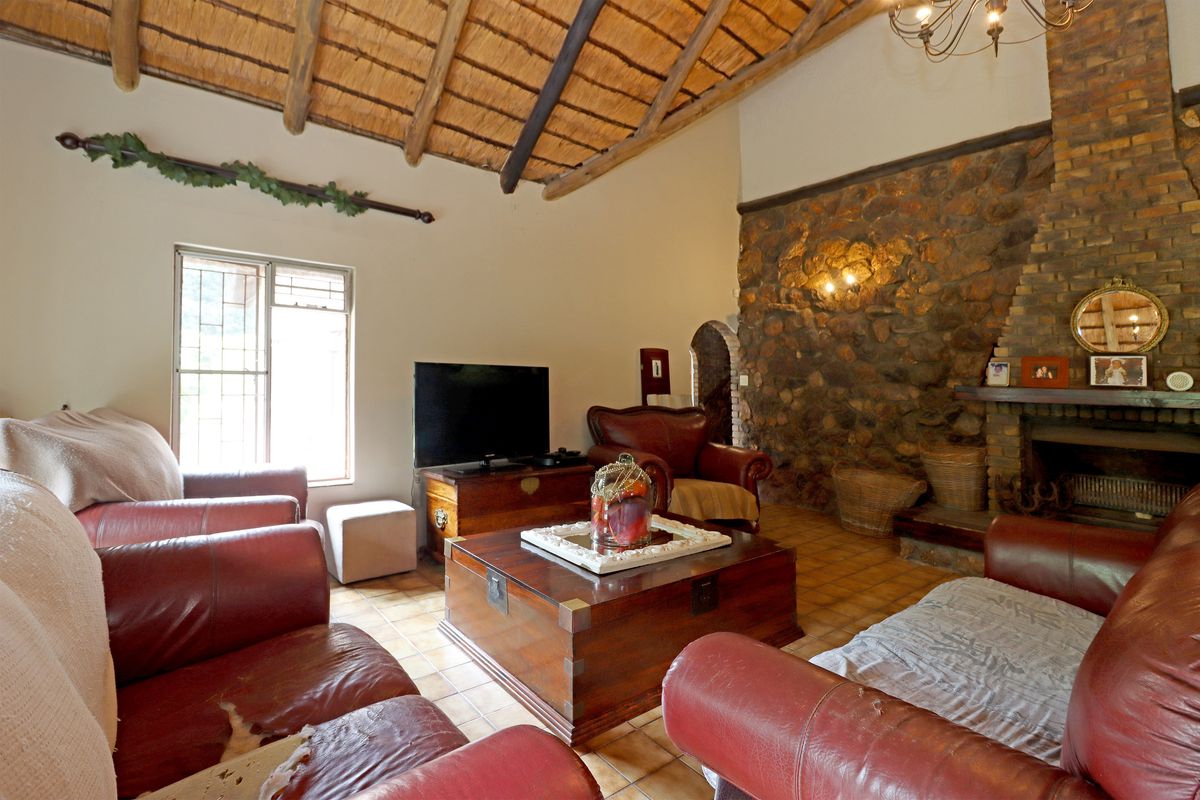 Spacious living room featuring a high vaulted thatched ceiling, exposed timber beams, and a prominent natural stone fireplace as a central focal point.