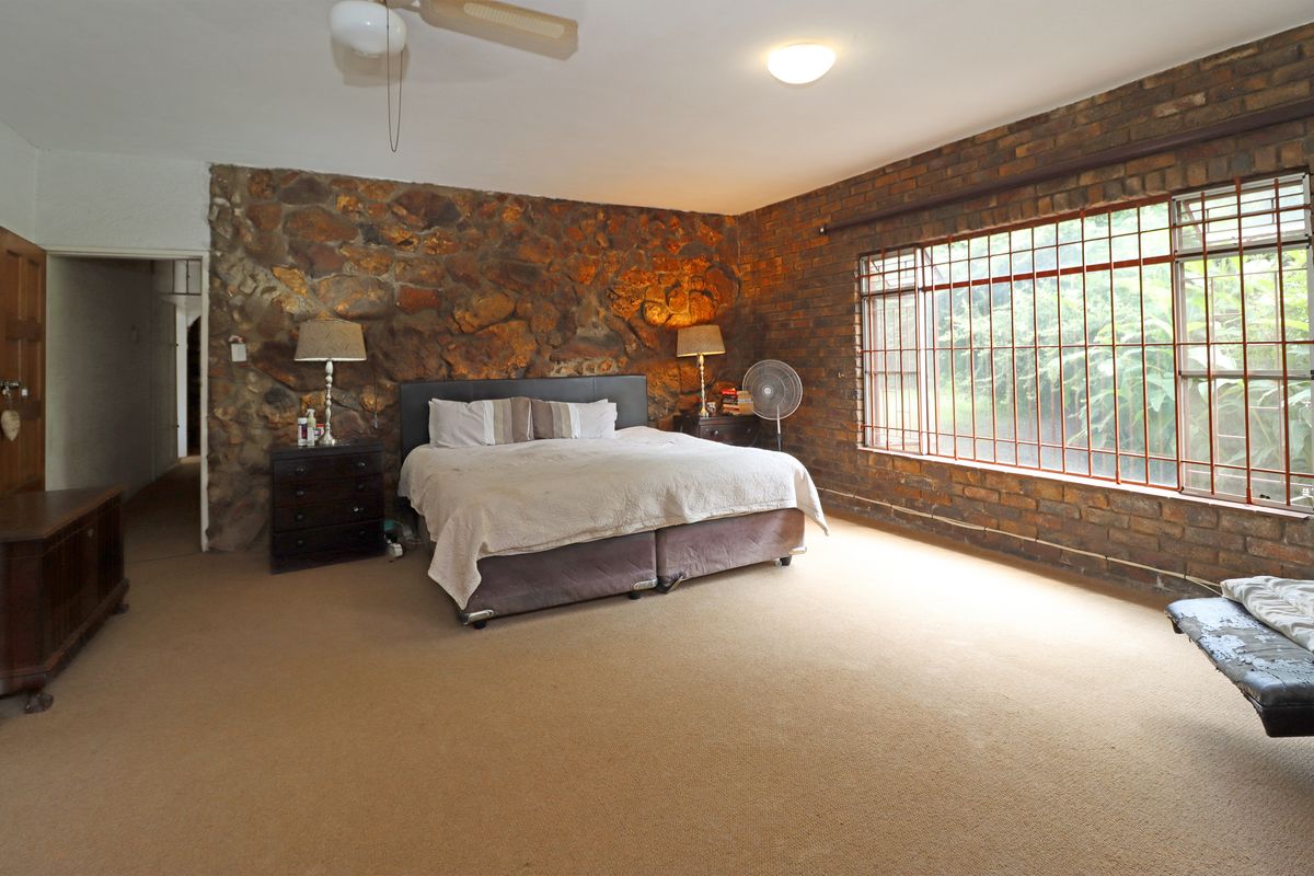Spacious bedroom featuring a rustic stone feature wall, exposed brickwork, and large windows with security bars.