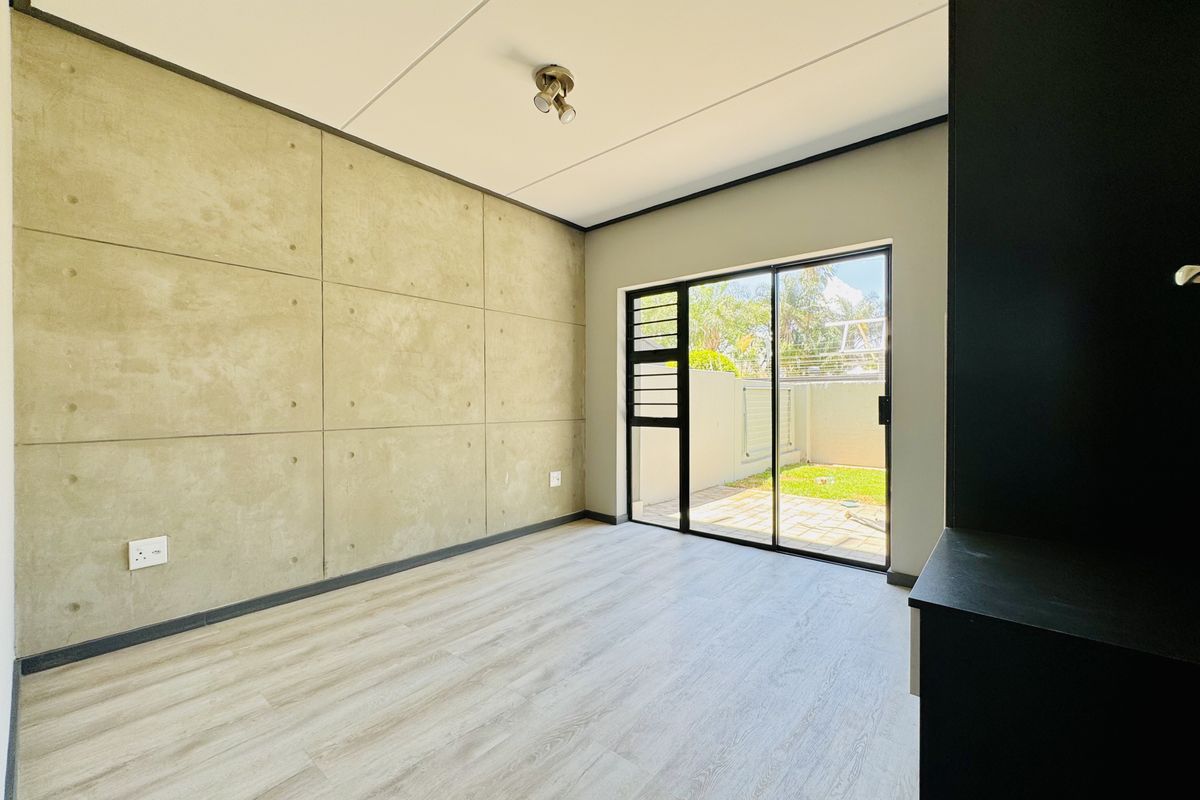 Modern living area featuring concrete-look feature wall, light wood-look flooring, and sliding glass doors providing direct access to a private patio and garden.