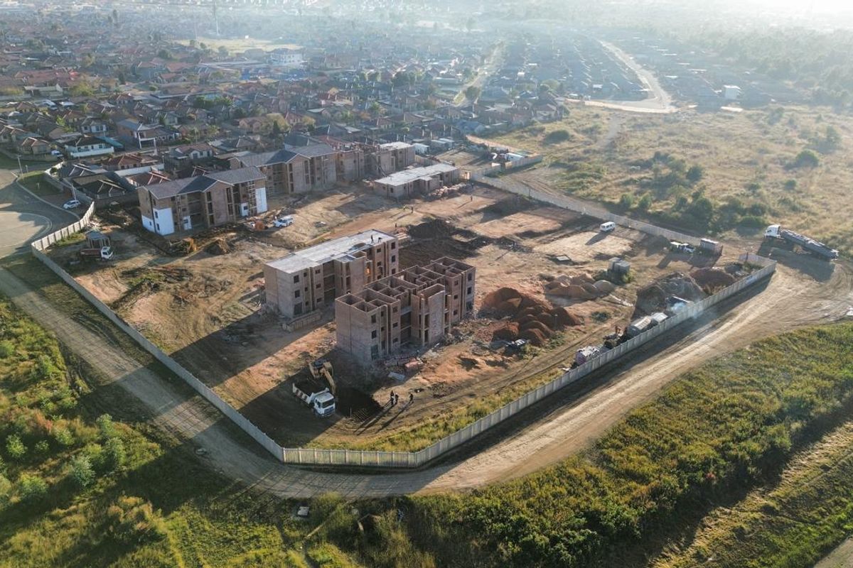 Aerial view of a residential development site showing multiple apartment blocks under construction with surrounding perimeter fencing.
