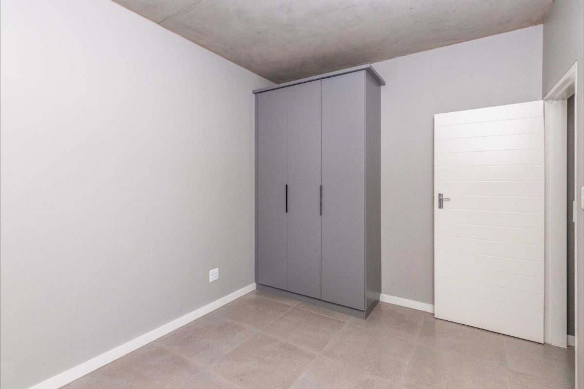 A clean, modern bedroom featuring neutral grey walls, tiled flooring, and a built-in grey wardrobe.