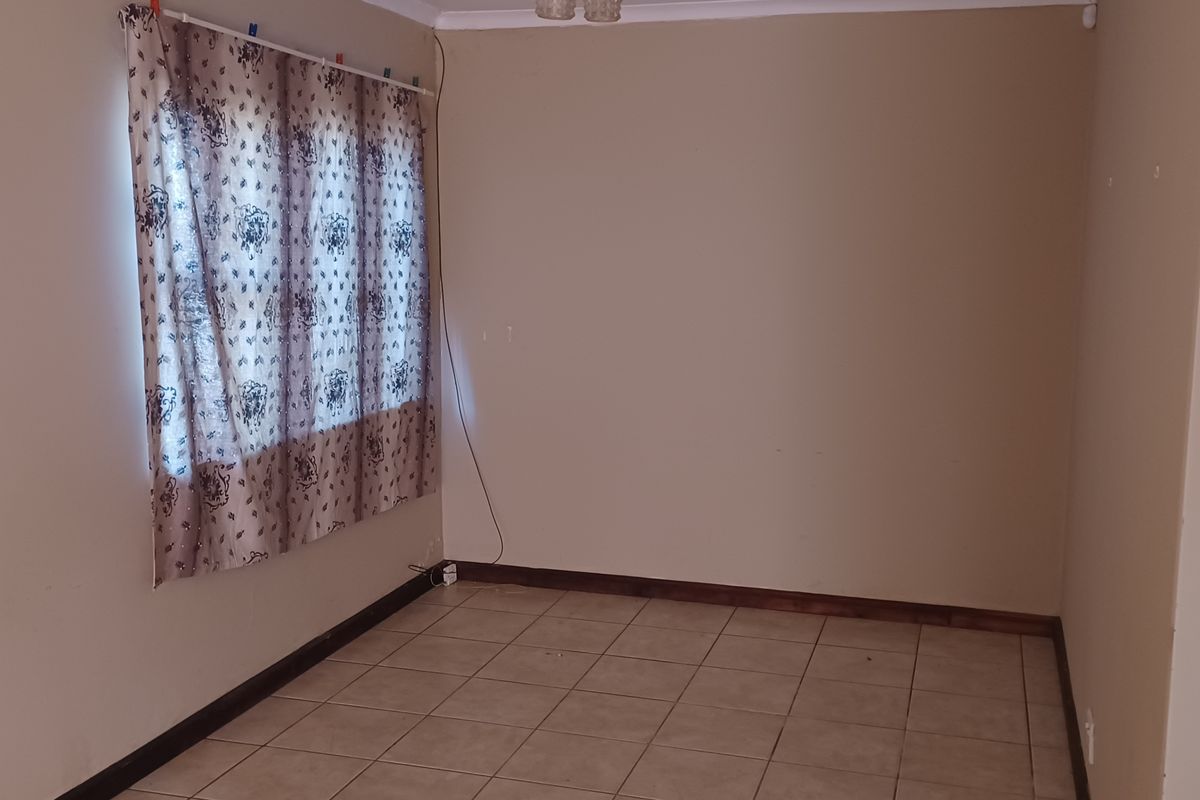 An empty living room featuring tiled flooring, neutral wall paint, and ceiling cornice, providing a blank canvas for potential interior design updates.