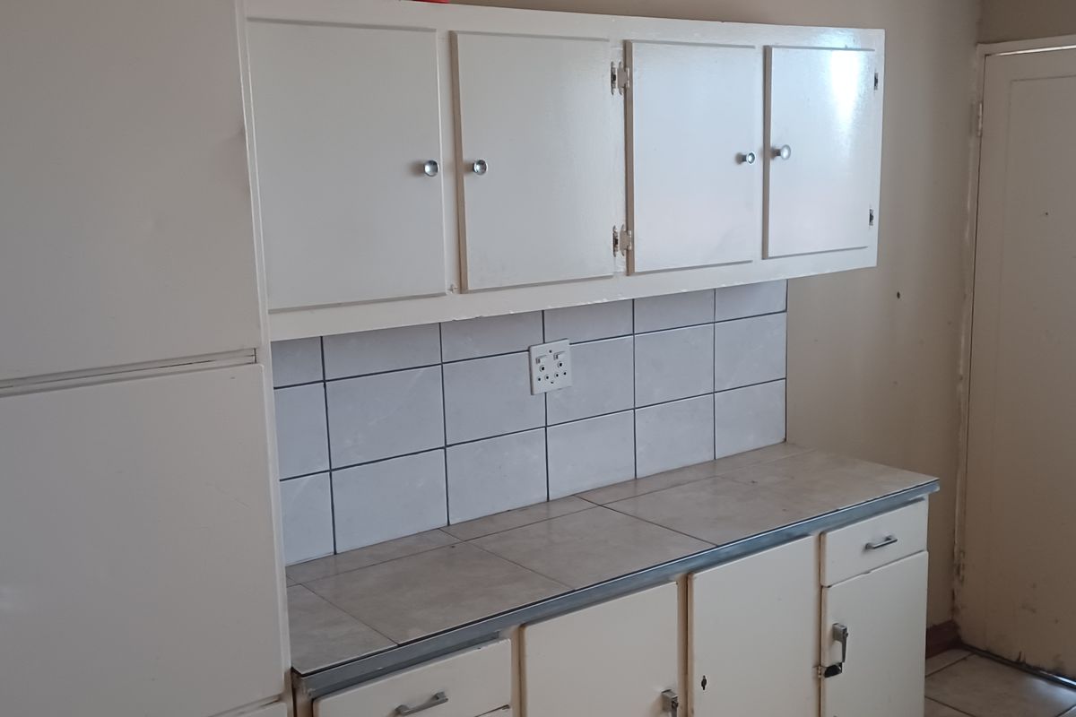 A dated kitchen featuring original built-in cabinetry, tiled countertops, and a tiled backsplash, offering a blank canvas for potential renovation and modernization.