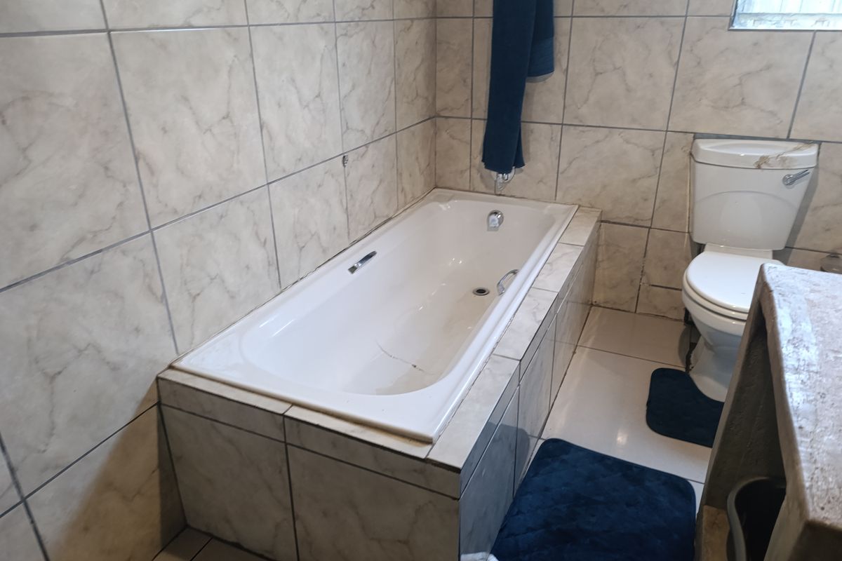 A functional bathroom featuring a built-in bathtub with tiled surround and a standard toilet, finished with neutral wall and floor tiles.