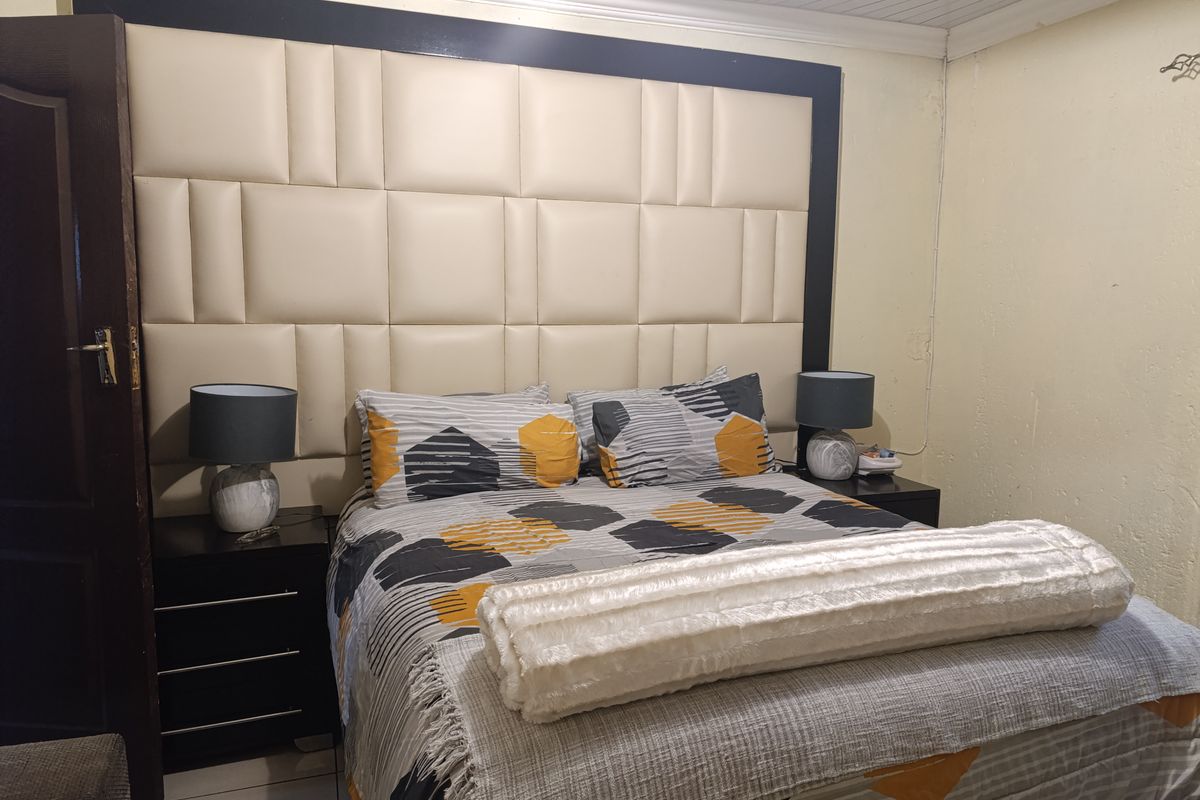 A bedroom featuring a large, custom-fitted upholstered headboard and tiled flooring.