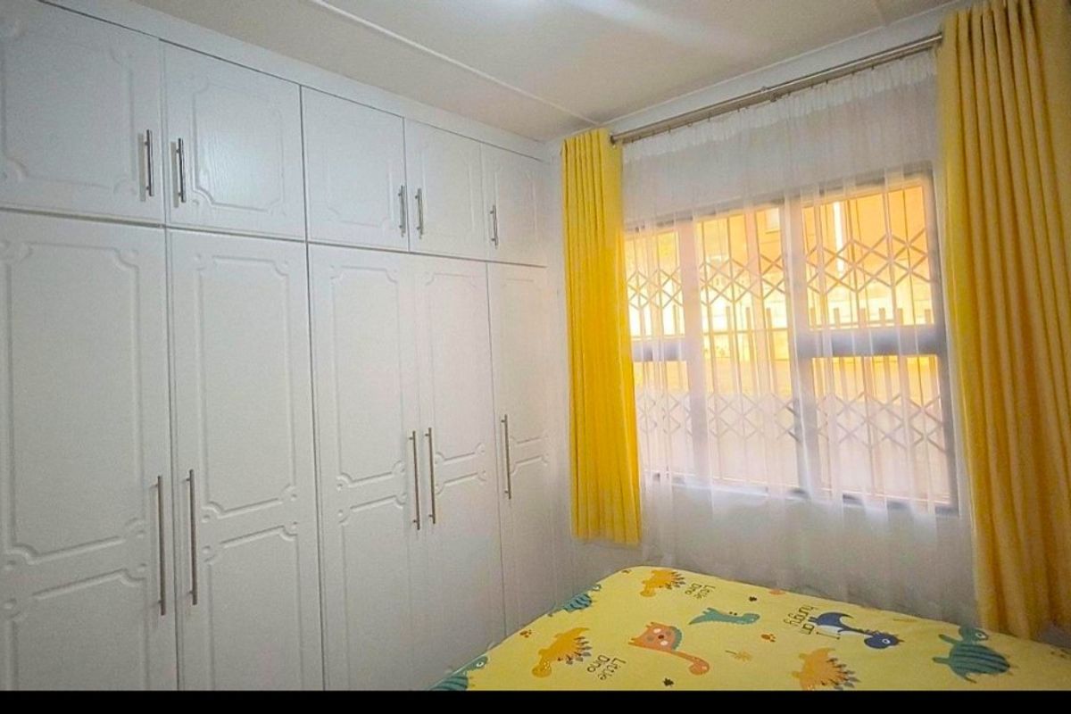 A well-maintained bedroom featuring extensive floor-to-ceiling built-in white cabinetry and a window fitted with security bars.