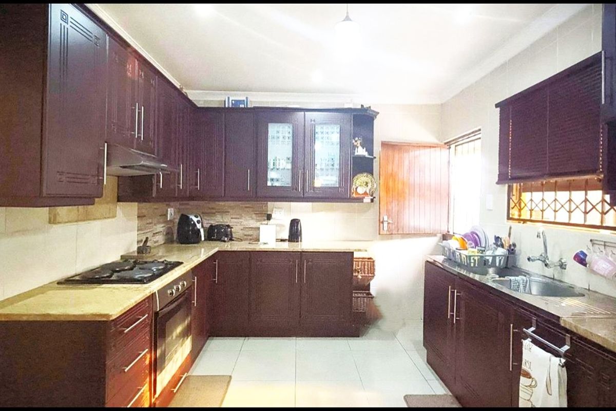 A functional kitchen featuring dark wood cabinetry, stone-look countertops, a built-in oven, gas hob, extractor fan, and a double sink.