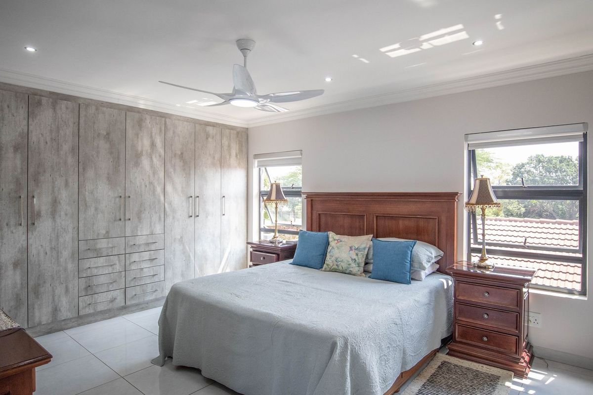 A well-maintained bedroom featuring extensive built-in cupboards, modern tiled flooring, a ceiling fan, and large windows providing natural light.