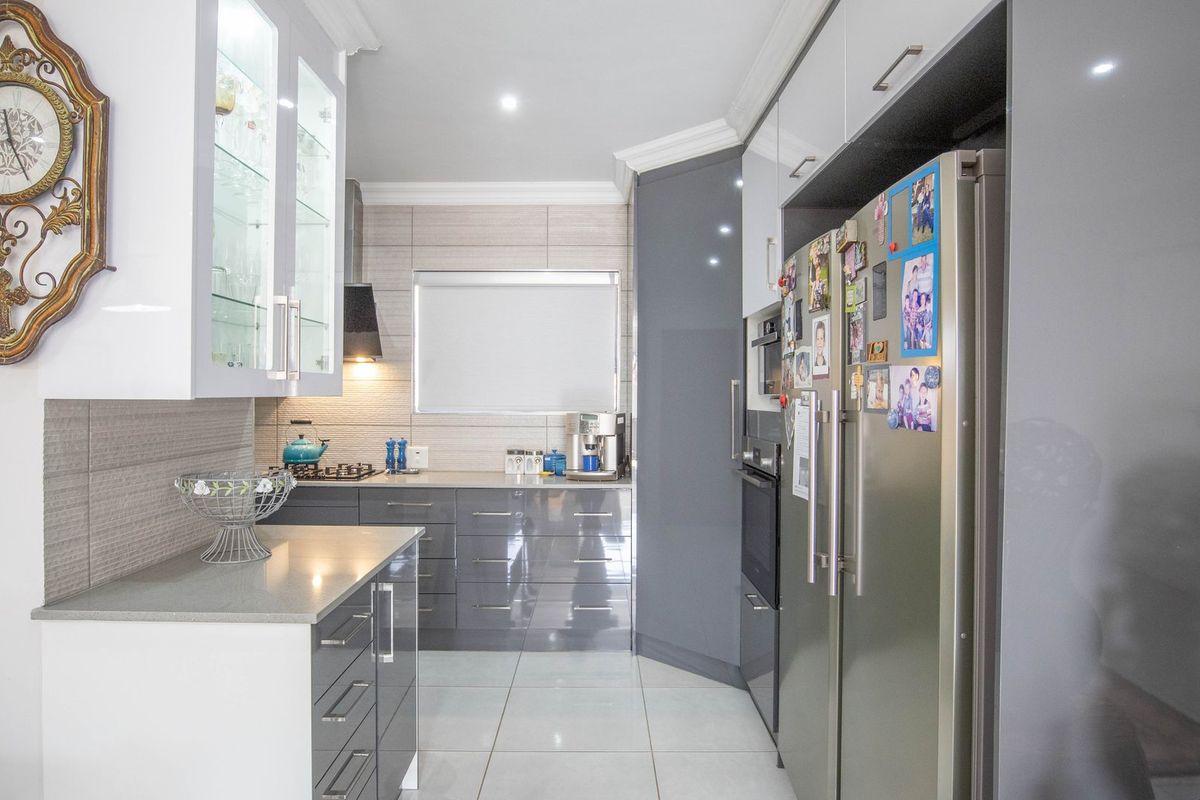 Modern kitchen featuring high-gloss cabinetry, stone countertops, integrated appliances, and sleek tiled flooring with recessed lighting.