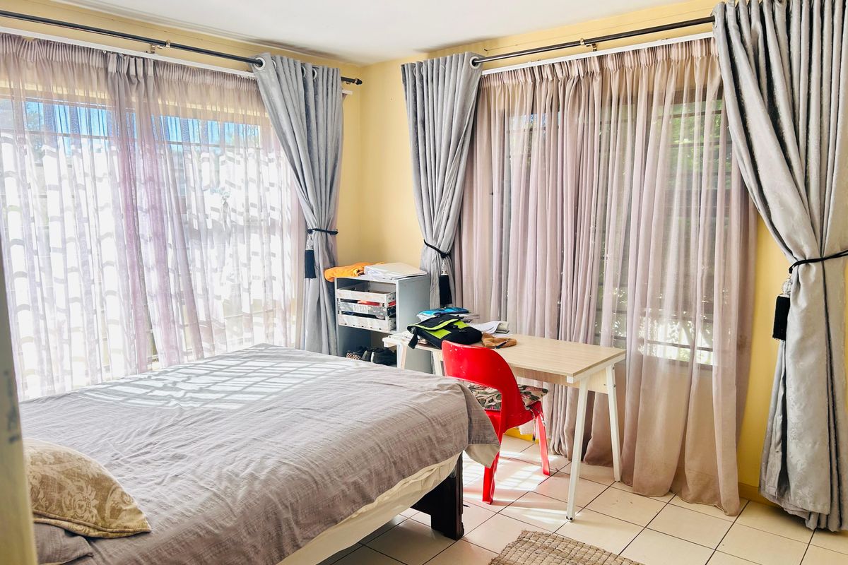 A bright bedroom featuring tiled flooring and large windows with floor-to-ceiling curtains, offering ample natural light.