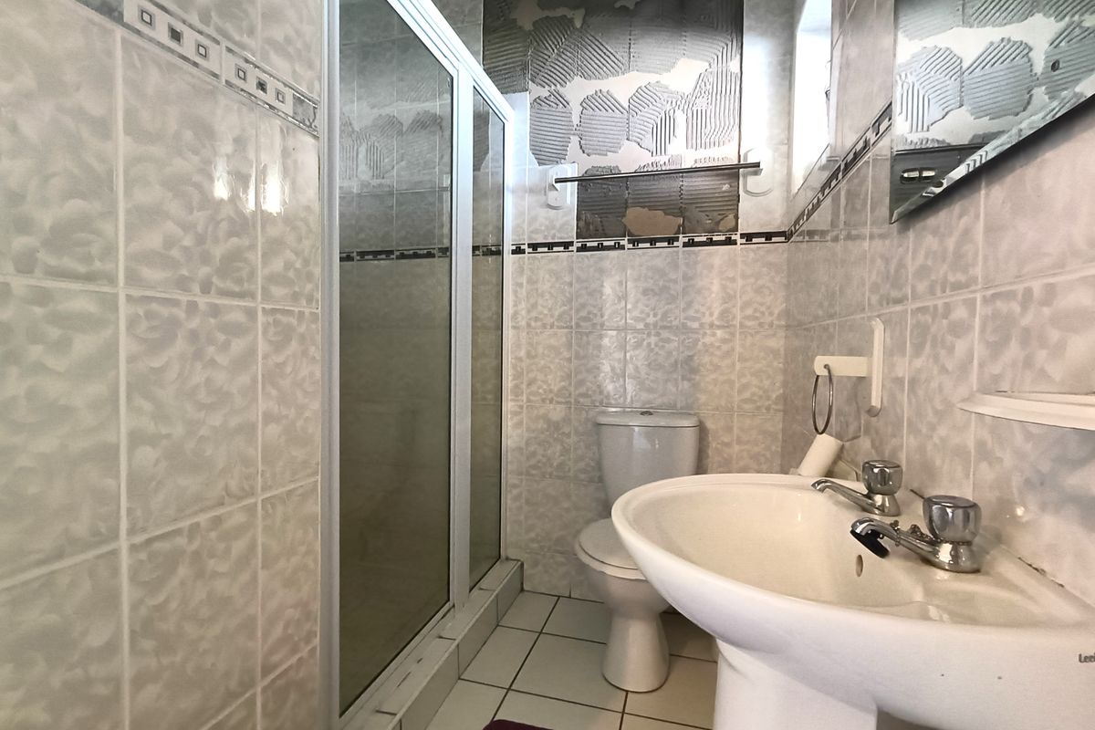 A bathroom featuring a pedestal basin, toilet, and shower enclosure, currently requiring repair due to missing wall tiles and exposed adhesive.