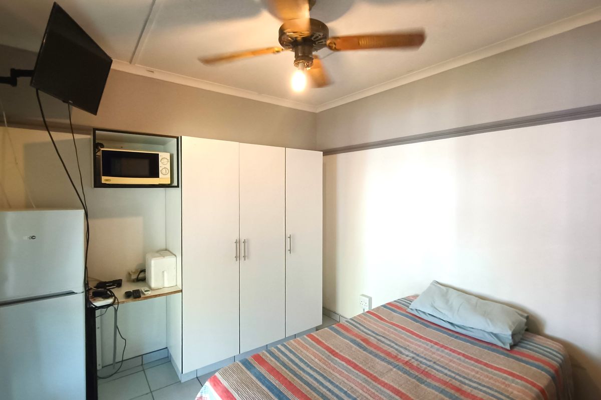 A functional bedroom featuring a built-in wardrobe, ceiling fan, and tiled flooring, with a dedicated alcove for a microwave and small appliance storage.