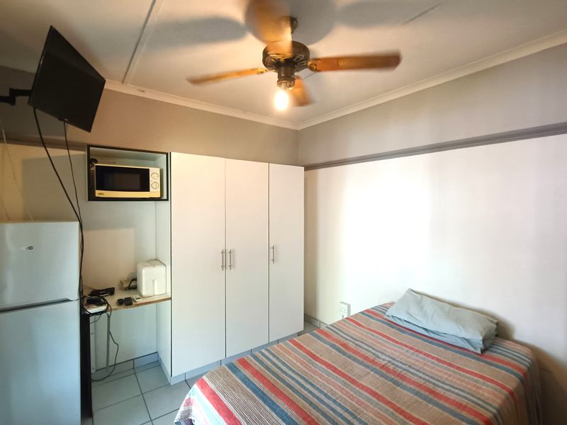 A functional bedroom featuring a built-in wardrobe, ceiling fan, and tiled flooring, with a dedicated alcove for a microwave and small appliance storage.