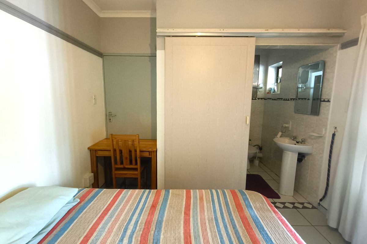 Bedroom featuring tiled flooring and an en-suite bathroom accessed via a sliding door, with a pedestal basin and neutral wall finishes.