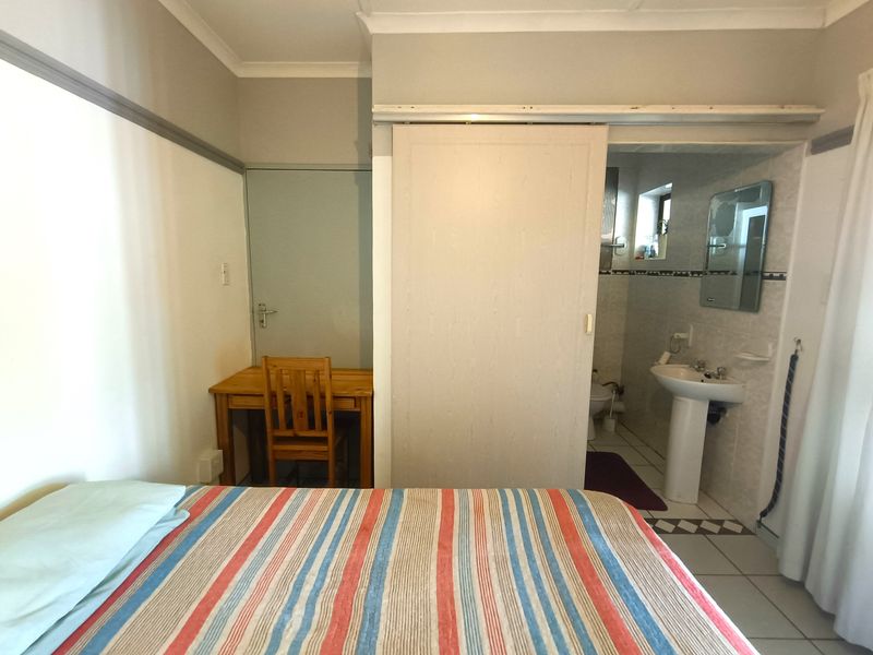 Bedroom featuring tiled flooring and an en-suite bathroom accessed via a sliding door, with a pedestal basin and neutral wall finishes.