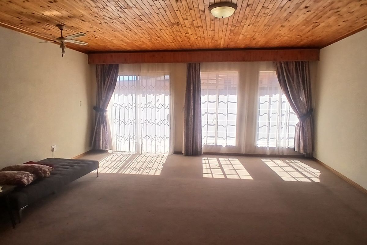 Spacious living room featuring a timber tongue and groove ceiling, ceiling fan, and large sliding glass doors with security gates leading outdoors.