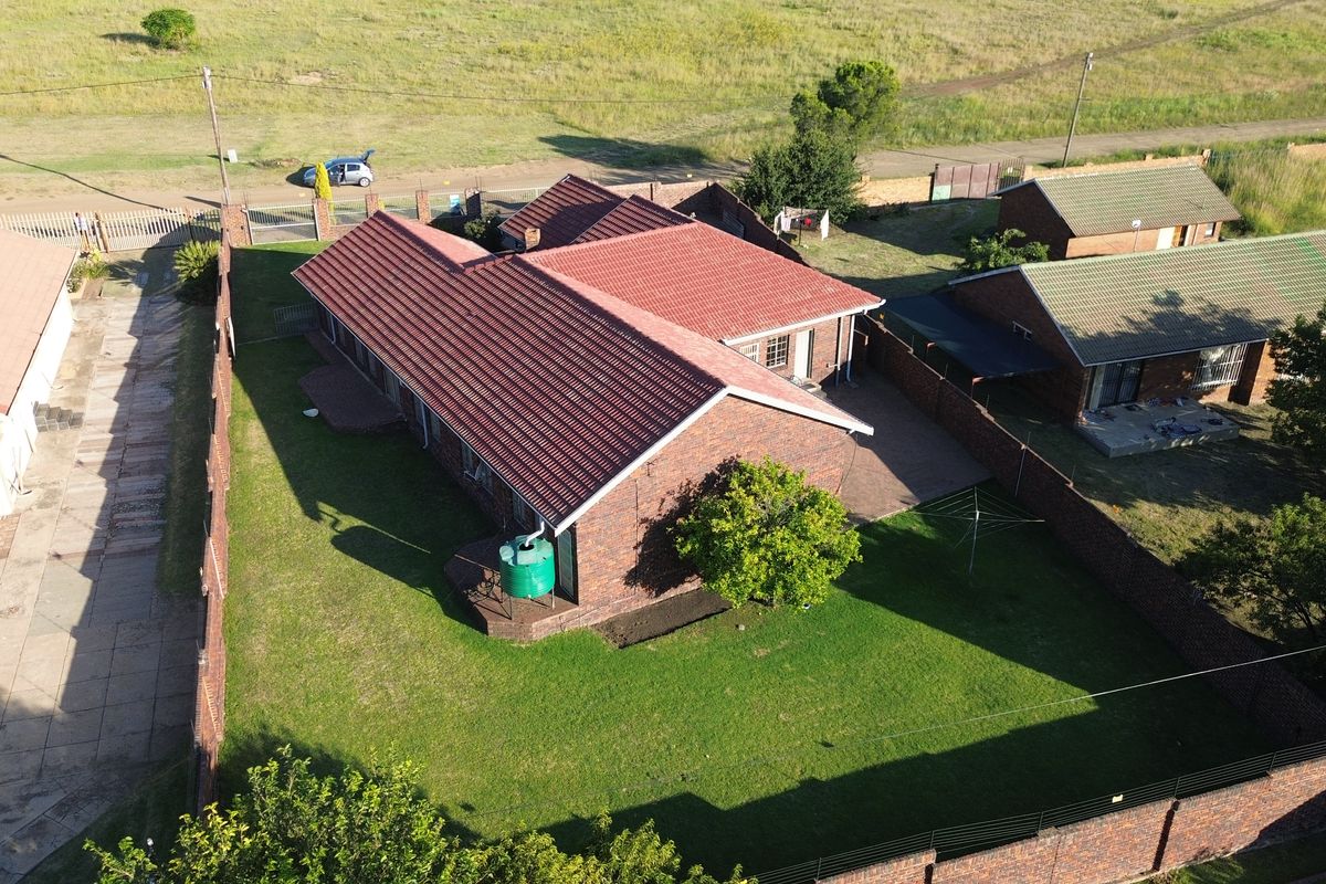 Aerial view of a brick house featuring a tiled roof, a private garden with a lawn, and a paved driveway area.