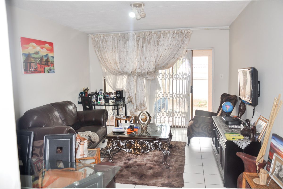A living room featuring tiled flooring and a sliding glass door with security gate leading to an outdoor area.