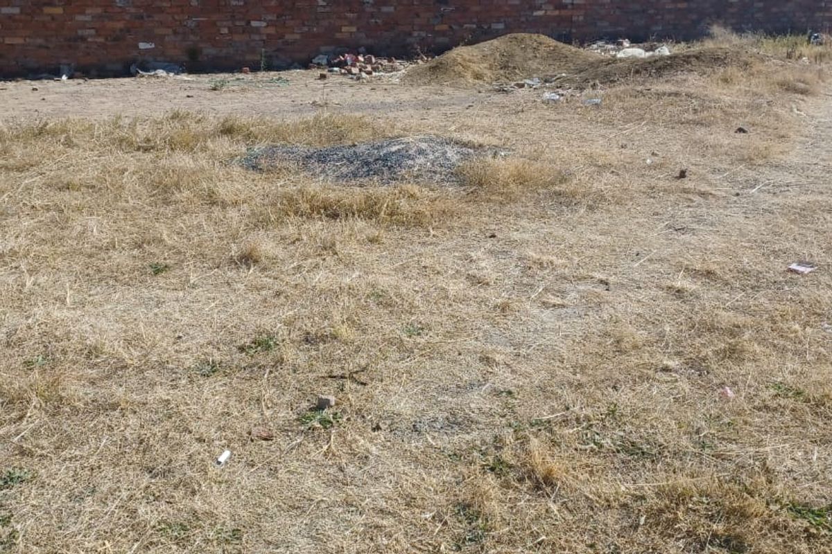 A vacant residential plot featuring dry grass, uneven terrain, and a perimeter brick wall, offering a blank canvas for future development.
