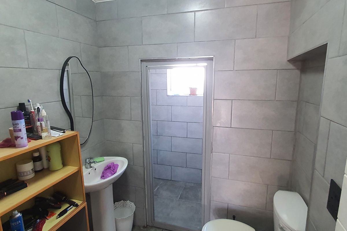 A functional bathroom featuring grey wall tiling, a pedestal basin, and a separate enclosed shower area with matching tile finishes.