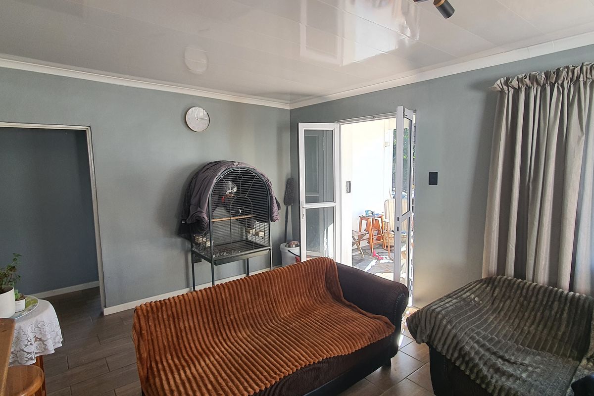 A living room featuring tiled flooring, a glossy ceiling finish, and double doors providing direct access to an outdoor patio area.