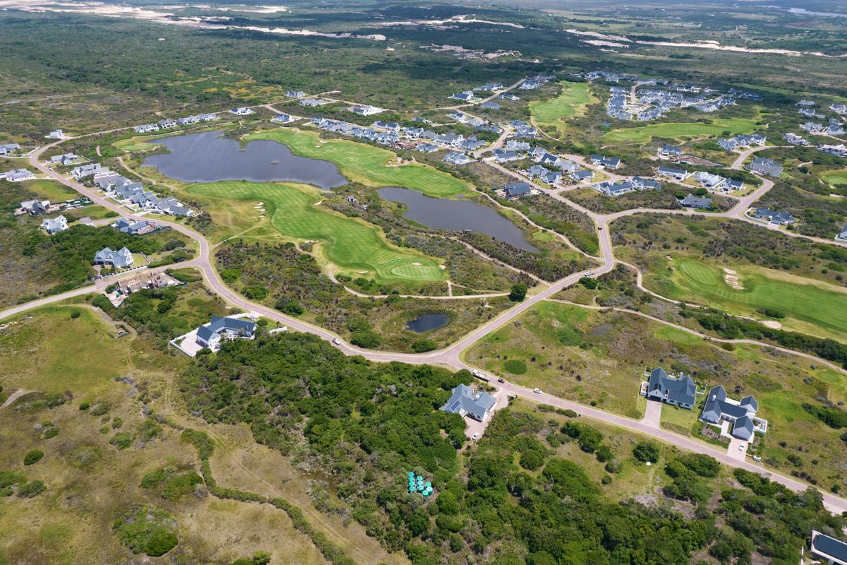 An aerial view of a residential estate featuring a golf course, natural lakes, and established road infrastructure within a coastal landscape.