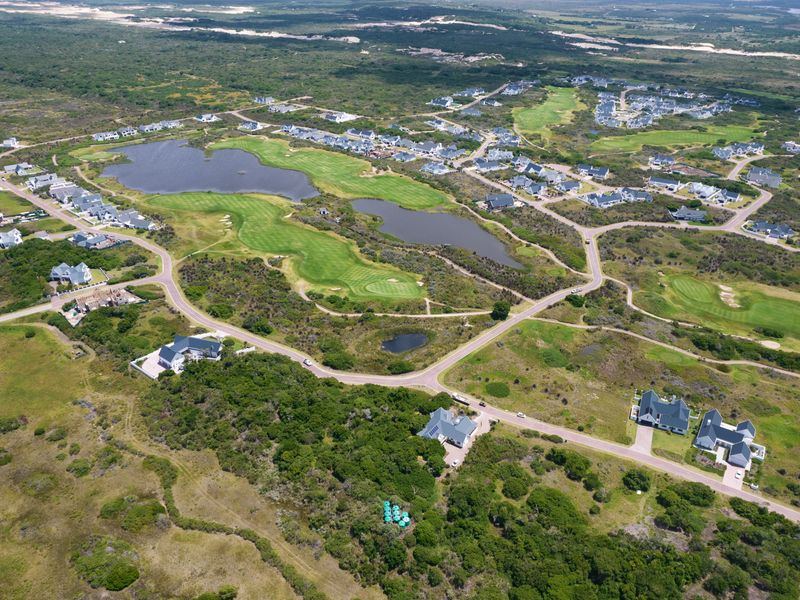 An aerial view of a residential estate featuring a golf course, natural lakes, and established road infrastructure within a coastal landscape.