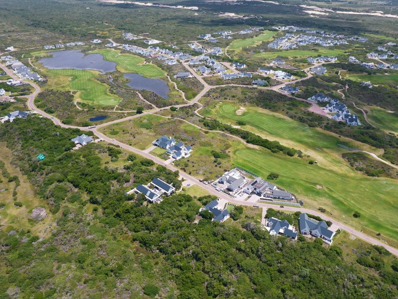 An aerial view of a residential estate featuring landscaped golf course fairways, water features, and established housing clusters within a natural coastal environment.