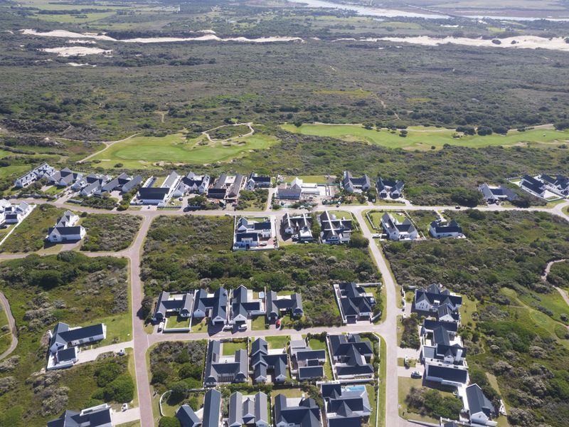 An aerial view of a residential estate featuring paved roads, modern housing, and proximity to a golf course and coastal landscape.