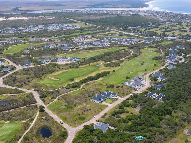 An aerial view of a residential estate integrated with a golf course, showcasing the surrounding coastal landscape and road infrastructure.