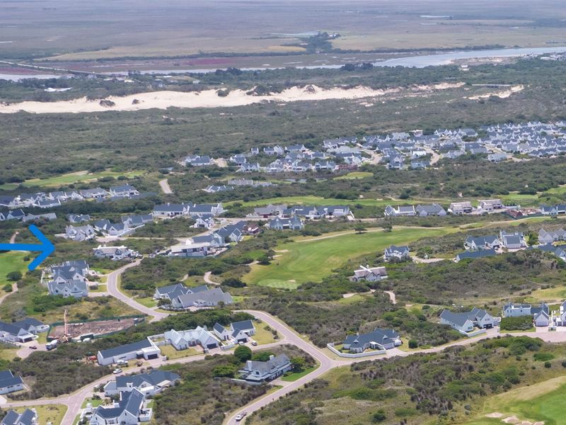 An aerial view of a residential estate situated within a coastal landscape, featuring proximity to a golf course and natural surroundings.