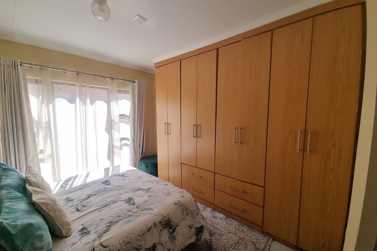 A bedroom featuring a large, light-wood built-in wardrobe with integrated drawers and tiled flooring, offering ample storage space.