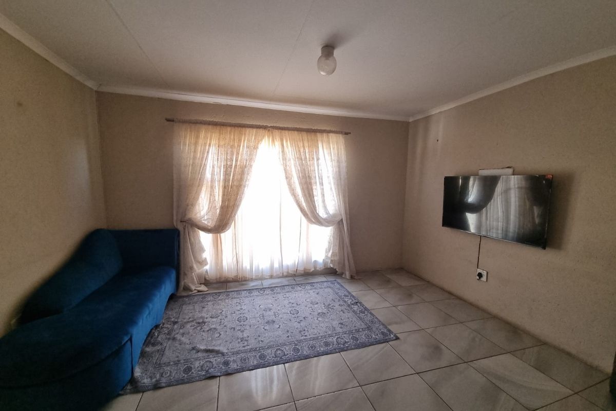 A simple living room featuring tiled flooring and natural light through window curtains.
