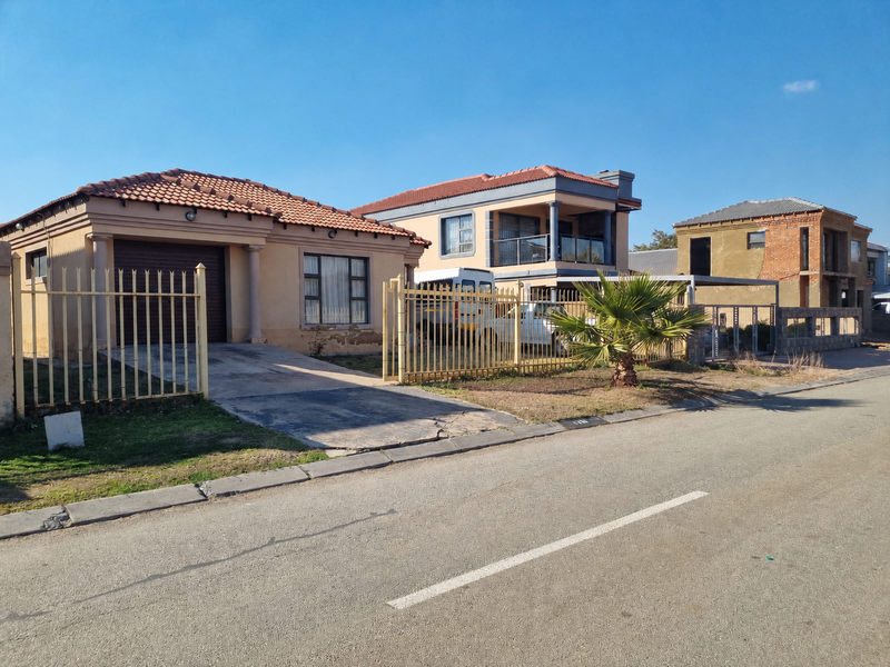 A street-level view of a residential property featuring a tiled roof, plastered exterior, and metal security fencing with a concrete driveway.