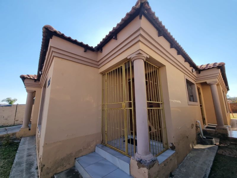 Front exterior view of a house featuring decorative columns, a security gate, and tiled roof, showing signs of exterior wear and paint deterioration.