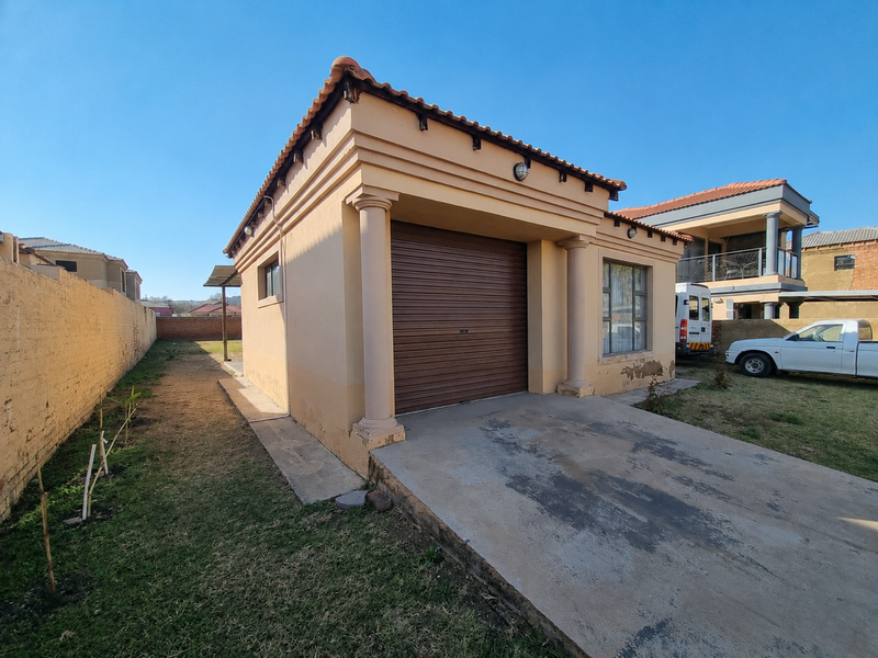 Detached single garage featuring a roll-up door, decorative columns, and a concrete driveway, situated on a residential plot with a boundary wall.