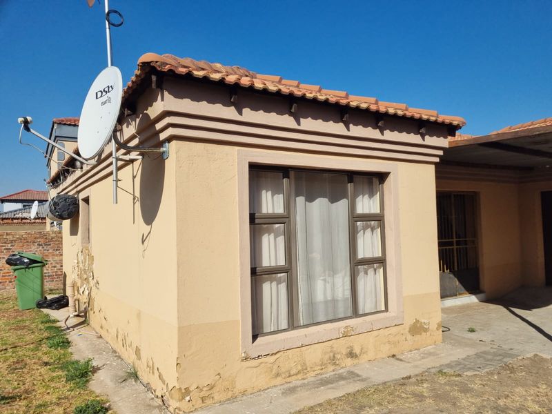 Rear exterior view of the property featuring terracotta roof tiles, aluminium window frames, and visible wear to the exterior plaster and paintwork.