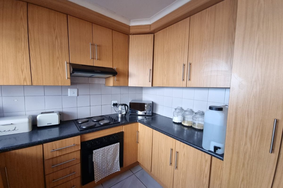 A functional kitchen featuring wood-look laminate cabinetry, dark countertops, a built-in oven, electric hob, and a tiled backsplash.