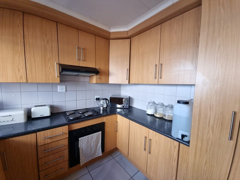 A functional kitchen featuring wood-look laminate cabinetry, dark countertops, a built-in oven, electric hob, and a tiled backsplash.